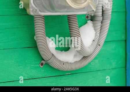 Covered with snow wires of old electricity usage meter on wall of green wooden house Stock Photo