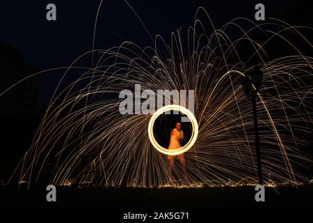 a long exposure photography of an steel wool on fire going in circles and dropping iron on ring fire as a shower