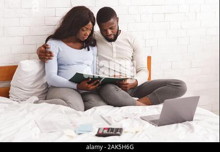 Young family budget concept. Upset expecting woman and her husband planning family budget, using calculator and laptop, taking notes, free space Stock Photo