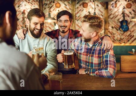Group of happy friends clinking glasses of beer at a table in a bar. Stock Photo
