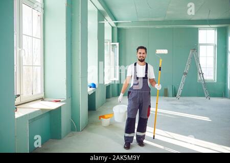Bearded painter smiling construction worker with tools on a construction site. Stock Photo