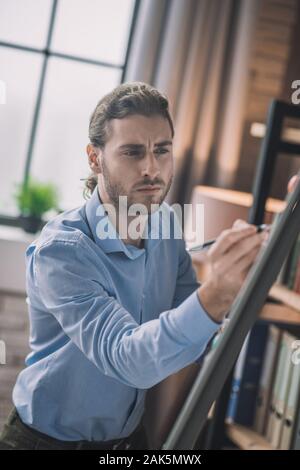 Making schemes. Young bearded man in eyeglasses writing on white board Stock Photo