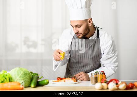 Fish Recipes. Male Chef Squeezing Lemon Juice On Roasted Salmon Steak Plating Dish In Kitchen Indoor. Selective Focus Stock Photo