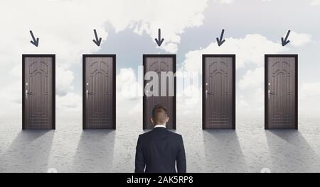 Choice concept. Rear view of businessman choosing the right door, each door indicated with arrow over sky background, panorama Stock Photo