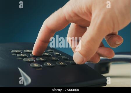 Closeup of male finger dialing a telephone number pressing button on black landline phone. Over blue background. Stock Photo