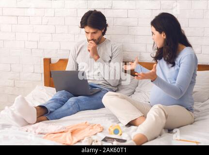 Pregnant woman blaming husband for not helping preparing things for maternity hospital, indifferent man playing games on laptop, free space Stock Photo