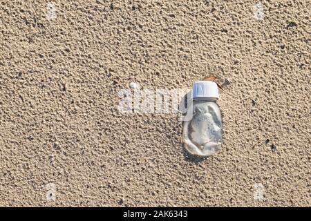 Small transparent container with the white cap is embedded in the sand after the rain. Stock Photo