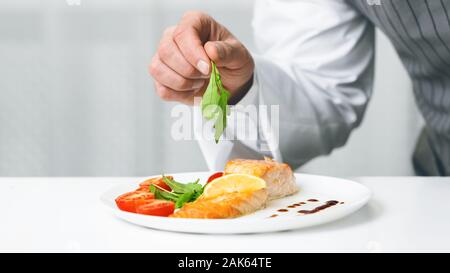 Fish Menu. Unrecognizable Chef Man Decorating Salmon Steak With Herbs Plating Dish In Restaurant Kitchen. Cropped, Panorama, Selective Focus Stock Photo