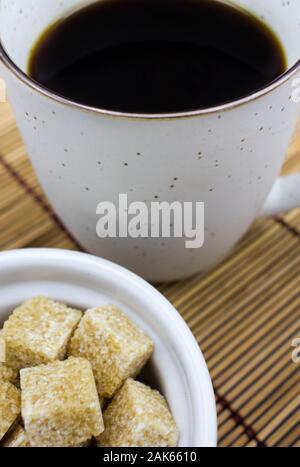 Close Up of Black Coffee in White Mug with Brown Sugar Cubes on Bamboo Mat Stock Photo