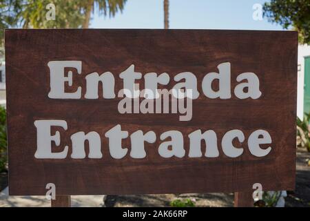 the Spanish and English word for -entrance- written on a big wooden sign Stock Photo