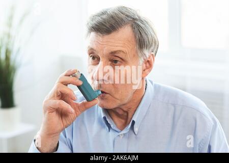 Senior Man Using Asthma Inhaler For Allergies In Modern Clinic, Copy Space Stock Photo