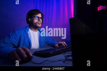 Gaming concept. Pro gamer playing shooter video game on personal computer all night Stock Photo