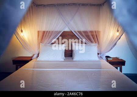 Luxury accommodation in tropical destination. Double bed with mosquito net in modern bungalow. Stock Photo