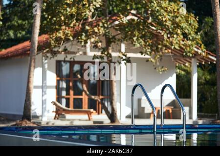 Luxury accommodation in tropical destination. Ladder to swimming pool against modern bungalow. Stock Photo