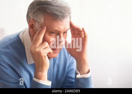 Headache Concept. Senior Gentleman Suffering From Migraine Pain Massaging Temples Sitting Over White Background. Selective Focus Stock Photo