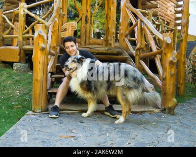 Young caucasian man petting a three legs Rough Collie dog. The man is sitting on a wood stairs. Love animals concept. Stock Photo