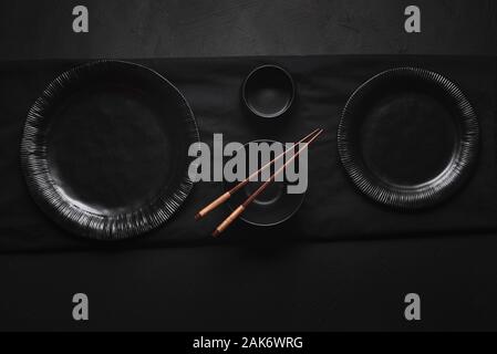 Empty dishes and bamboo chopsticks on black table. Above view of all black tableware. Japanese table settings. Asian dinner settings. Food background. Stock Photo