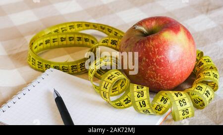 diet concept, close-up red apple with measuring tape and notebook with pen on the table Stock Photo