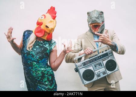 Crazy senior couple wearing chicken and t-rex mask while dancing outdoor - Mature trendy people having fun celebrating and listening music Stock Photo