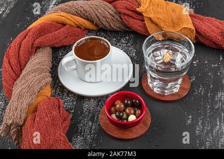 Traditional Turkish coffee in ceramic cup on black wood table. Served on the table with a glass of water and chocolates. Stock Photo