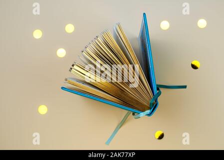 An open diary or a book with gold pages. On a beige background with scattered sequins. Stock Photo