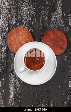 Traditional Turkish coffee in ceramic cup on black wood table. Served on the table with a glass of water and chocolates. Stock Photo
