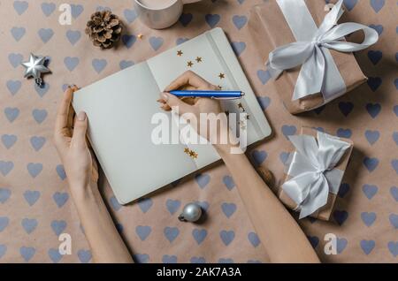 Female writing wish list in to notebook near gifts Stock Photo