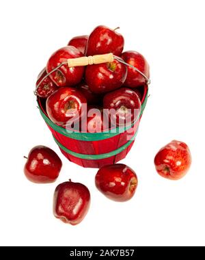 Vertical shot of a red bushel basket with green bands full of red shiny apples with a few that fell on the floor in front of it. Stock Photo