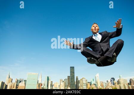 Levitating businessman holding his arms out for balance while floating cross-legged above the city skyline Stock Photo