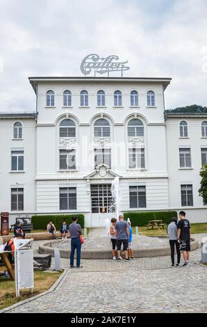 Broc, Switzerland - July 27, 2019: People waiting in front of the building of the famous Cailler chocolate factory. Visitors in the outside courtyard. Tour and museum. Swiss chocolate. Vertical photo. Stock Photo