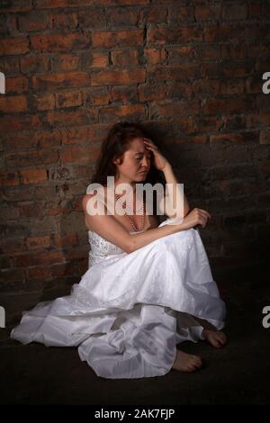 September 2019 - Sad depressed young red headed woman wearing a wedding dress in the studio, in Bristol. Stock Photo