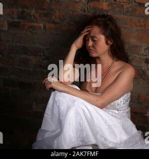 September 2019 - Sad depressed young red headed woman wearing a wedding dress in the studio, in Bristol. Stock Photo