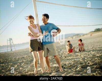 Smiling couple standing next to a volleyball net on a sandy beach. Stock Photo