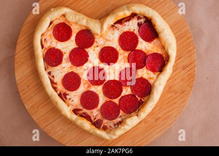 Pizza heart shaped with pepperoni on wooden background. Concept of romantic love for Valentines Day . Love food Stock Photo