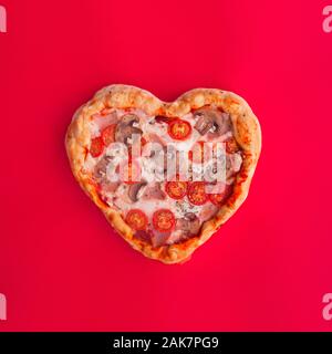 Pizza heart shaped with ham tomatoes and mushrooms on red background. Concept of romantic love for Valentines Day . Love food Stock Photo