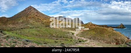 An horizontal panoramic view of Cabo de Gata, in Almería. A mountain is in the left and the sea in the right. A road goes to some houses. Stock Photo