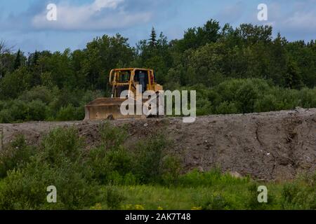 A front view of an old rusty tractor equipped with a blade, known as a bulldozer, parked on farmland with green trees in background and copy space Stock Photo