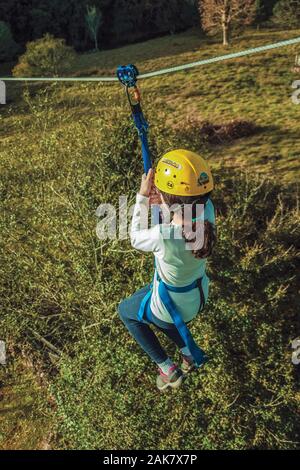 Girl descending by cable in a zip-line over meadows and trees on a valley near Bento Goncalves. A wine producing country city in southern Brazil. Stock Photo