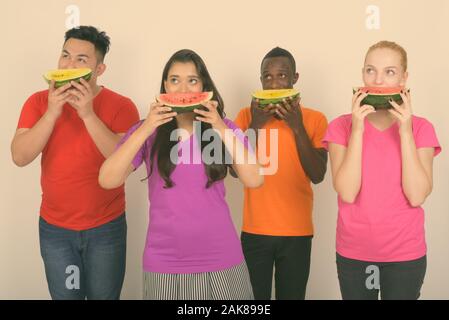 Studio shot of diverse group of multi ethnic friends thinking while covering face with slice of watermelon together Stock Photo