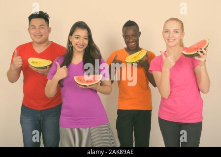 Studio shot of happy diverse group of multi ethnic friends smiling while holding slice of watermelon and giving thumb up together Stock Photo