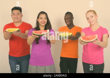Studio shot of happy diverse group of multi ethnic friends smiling while giving slice of watermelon together Stock Photo