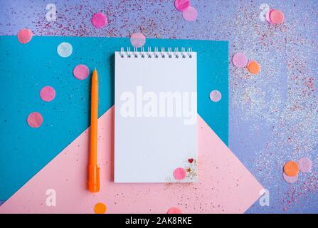 Flat lay of note pad and pencil on multicolored background with glitter and confetti. New year resolutions concept. Stock Photo