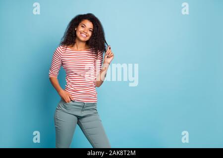 Photo of amazing pretty dark skin lady with adorable smile holding hands in pockets playing with curl wear casual street clothes isolated pastel blue Stock Photo
