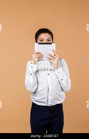 Emotional schoolboy holding digital tablet in front of his face. the child is afraid of the real world and lives in a virtual world Stock Photo