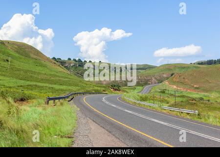 Scenic asphalt road travel route winding through valley and green hills blue sky clouds summer landscape. Stock Photo