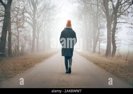 Back view of a woman walking into the distance on a foggy road Stock Photo