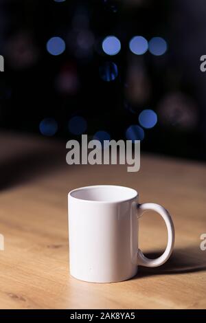 White coffee mug isolated on a wooden table on a dark background with spotlights Stock Photo