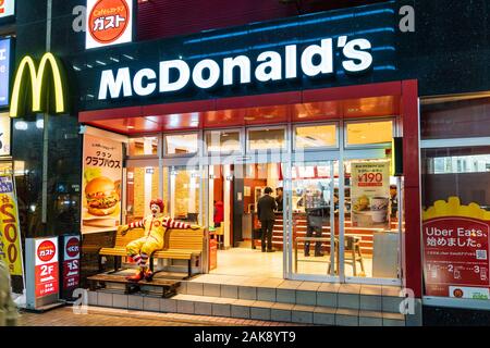 Small McDonalds in Motomachi, Kobe, Japan. Night time view of exterior of entrance looking into to counter with customers being served. Stock Photo