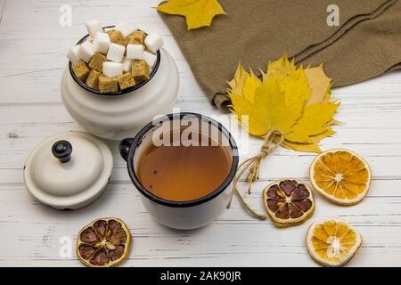 tea in an aluminum cup and sugar in cubes in an aluminum sugar bowl, brown scarf, maple leaves, dried oranges and dried lemon on a light wooden backgr Stock Photo