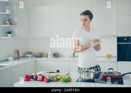 Portrait of his he nice attractive serious focused guy learning making lunch writing notes plan buyings at light white modern style interior house Stock Photo